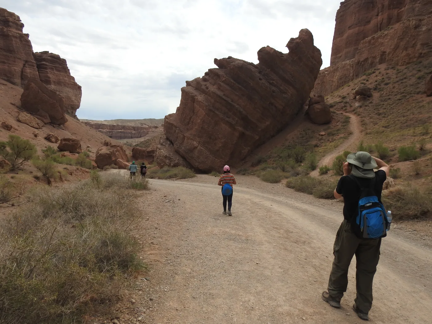 Travelers walking a canyon track past a huge tilted rock