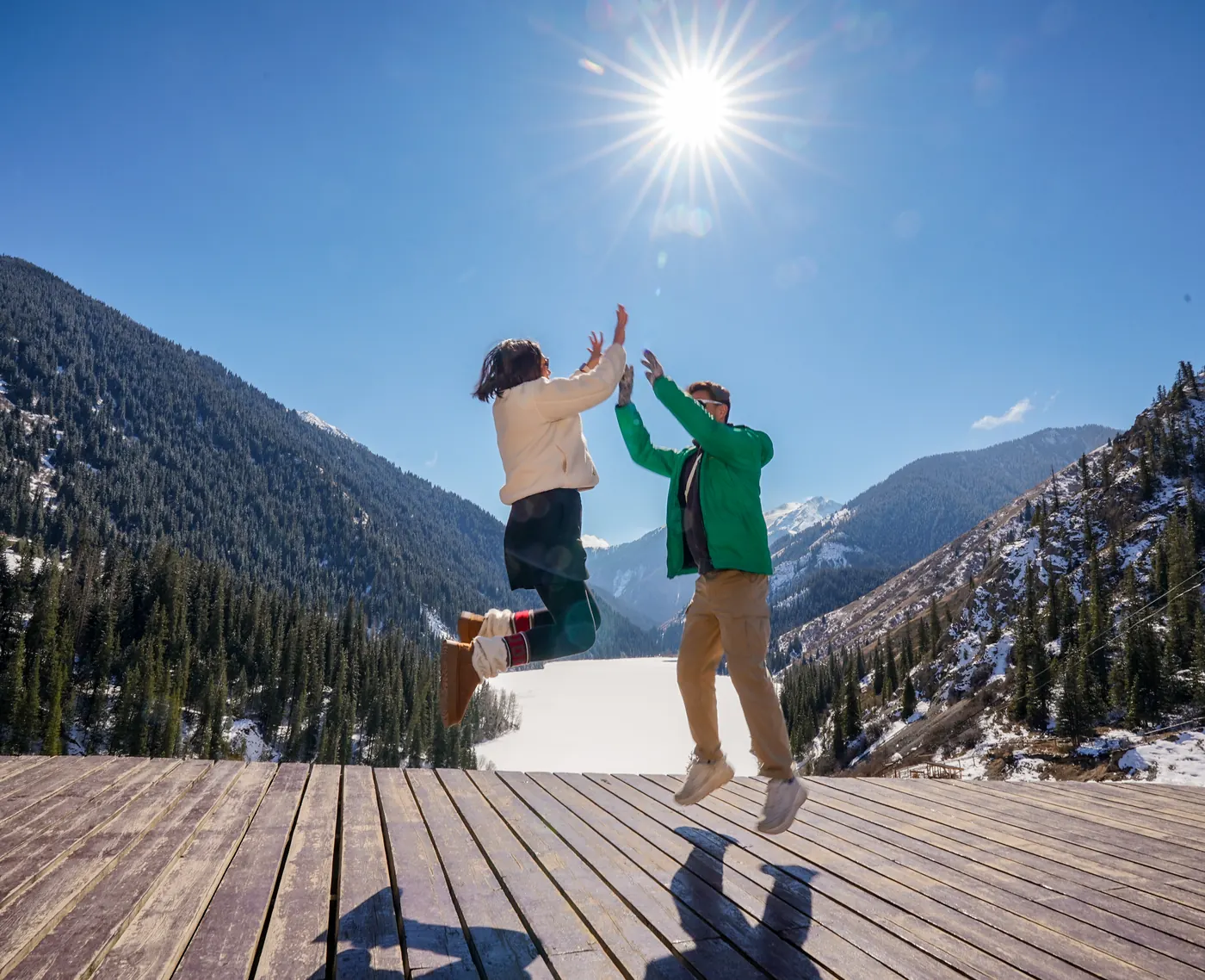 Two travelers jumping for a high five on a mountain deck