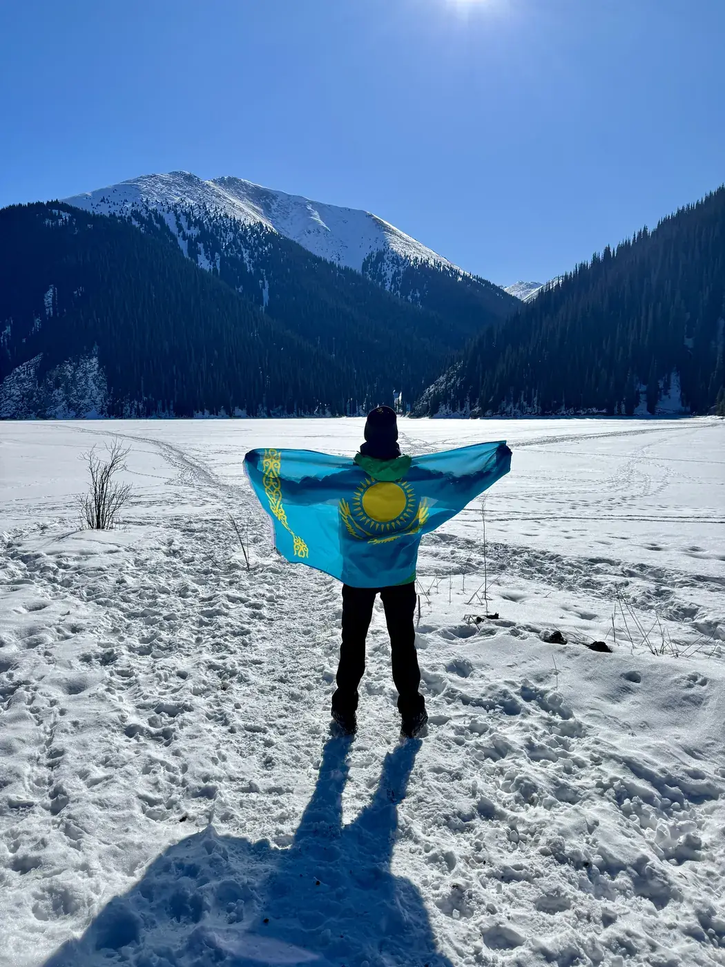 A traveler holding the Kazakh flag on a snowfield in the mountains